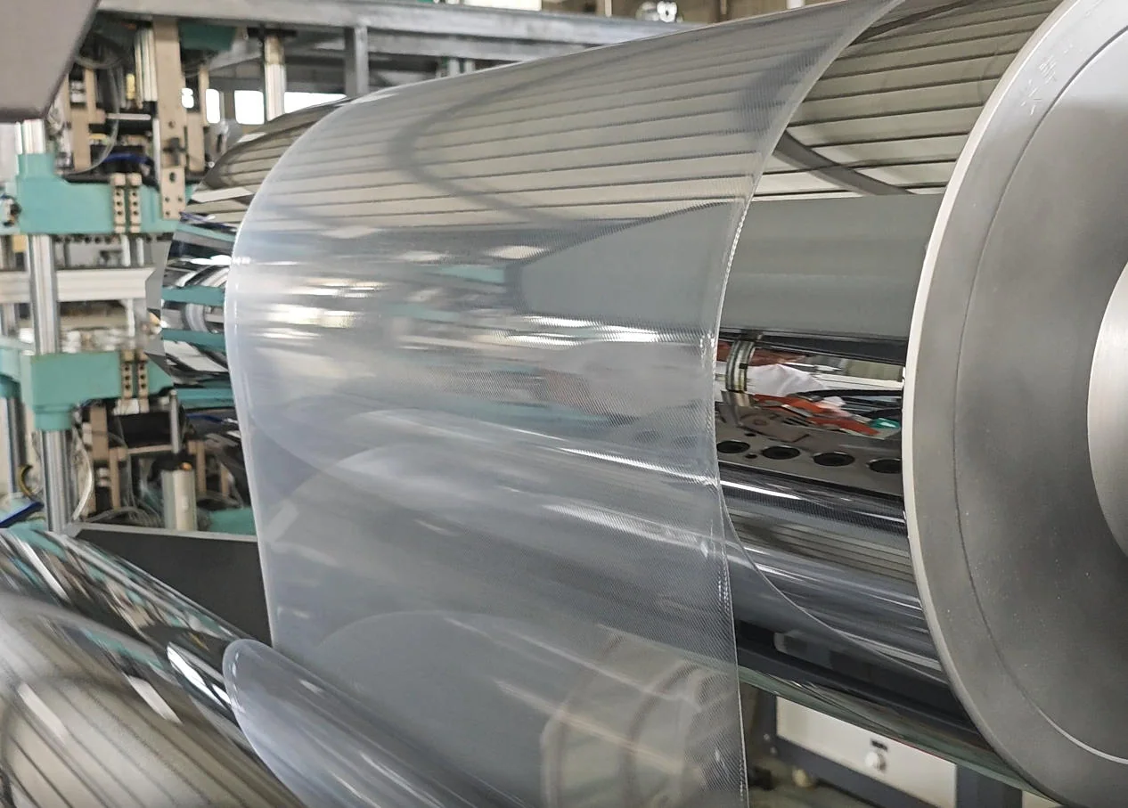 Clear plastic sheet being processed through production rollers